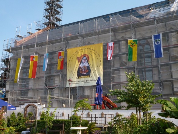 Das aufgehängte Bild der Hl. Hildegard am Gerüst der Kirche mit den Fahnen der einzelnen Ortsgemeinde.