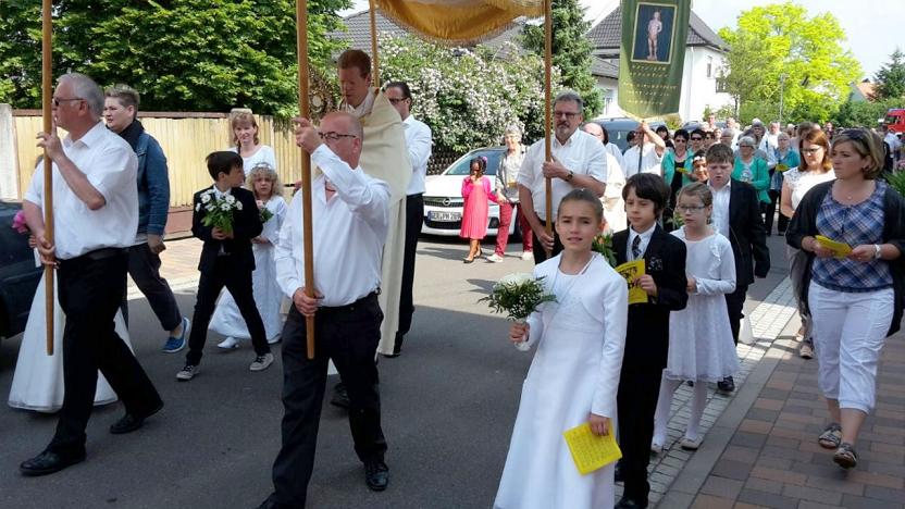 Das "Allerheiligste" in der Monstranz, getragen von Pfarrer Alexander Pommerening und begleitet von den Kommunionkinder und um im Hintergrund der Kath. Kirchenchor mit der Fahne vom hl. Sebastian