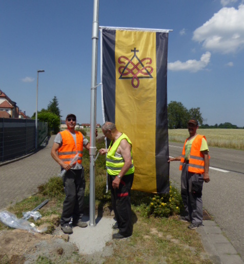 Mitarbeiter der Gemeinde bei der ersten Hissung der neuen Fahne an der Einmündung Tongruben/Jockgrimer Straße. Fotos: Beil