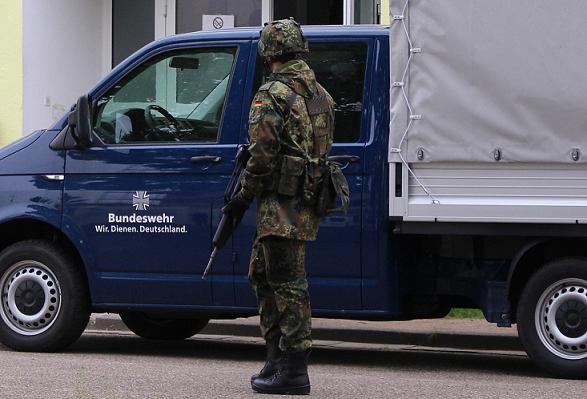 Soldat mit Waffe vor einem Bundeswehr-LKW mit der Aufschrift Wir. dienen. Deutschland.