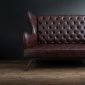 Sofa of black leather standing in center on concrete floor against dark grey wall with copy space. Vintage brown leather sofa with grunge gray wall living room.