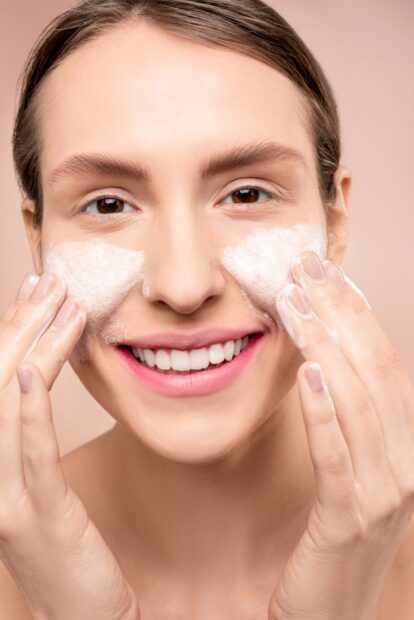 Junge Frau lächelt bei der Reinigung ihrer Gesichtshaut